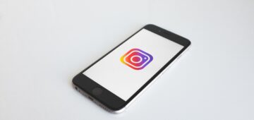 Ein schwarzes Smartphone liegt auf einem weißen Untergrund. Auf dem Smartphone ist das Logo von Instagram abgebildet.